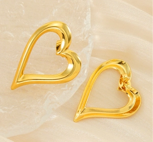 Close-up of gold hollow heart earrings on beige silk fabric with reflective glass texture