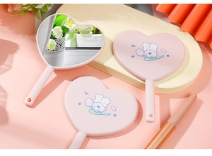 Detail view of heart-shaped handheld mirrors with cute cartoon prints and pink frames