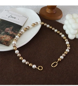 Detail of gradient pearl necklace with gold ring clasp on dark velvet background