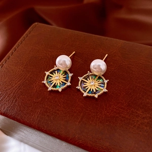 Detail of 18k gold plated pearl earrings with star compass charms on leather surface