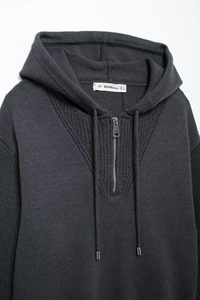 Detail of dark grey knit hoodie with half-zip closure and ribbed texture details