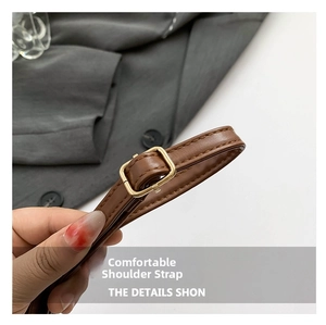 Detail of adjustable brown leather shoulder strap with a polished gold metal buckle