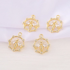 Macro shot of four golden honeycomb bee pendants with sparkling zircon on white silk