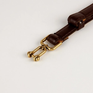 Detailed view of dark brown leather strap with polished golden horseshoe metal buckle