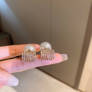Detail view of gold geometric earrings with pearls and pavé rhinestones held by hand