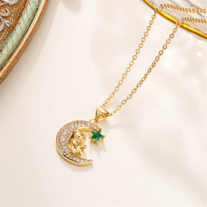 Detail of gold crescent moon pendant featuring a small bear and green star gem