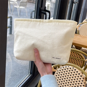 Detail of soft cream corduroy makeup bag with vertical stripes and stitched brand label