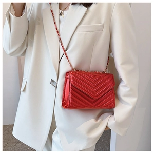 Detail of red quilted patent leather crossbody bag with chain strap on a model