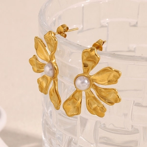 Exaggerated 18K gold plated flower earrings with pearls shown on a textured glass