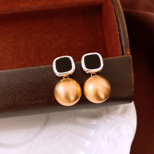 Detail view of matte gold ball earrings with black acetate square studs on a ceramic plate