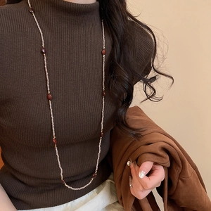 Close-up of ethnic tiger eye beaded necklace layered on a dark brown sweater