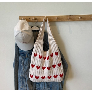 Detalle del bolso de punto con estampado de corazones junto a una chaqueta vaquera y gorra
