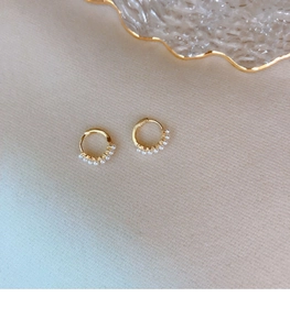 Close-up of gold hoop earrings with five delicate pearls on a beige textured cloth