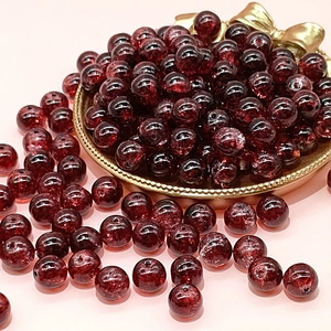 Detailed macro view of 10mm dark red cracked glass beads in a gold metal tray