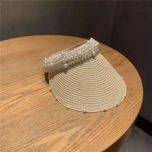 Detail of a beige straw visor hat with multi-layer pearl embellishments on the brim