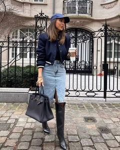 Street style view of a navy bomber jacket paired with a denim skirt and high leather boots