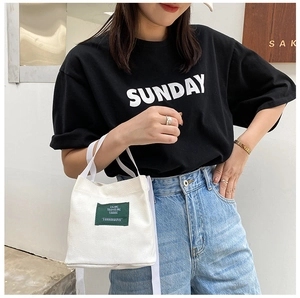 Detail of a white canvas mini bucket bag featuring a green woven logo and shoulder strap