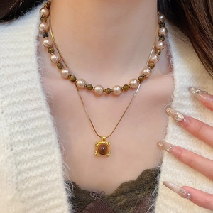 Close-up of a layered necklace featuring tiger eye stones, pearls and a golden square pendant