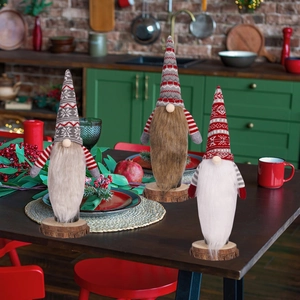 Three festive Christmas gnome decorations with knitted hats on round wooden bases