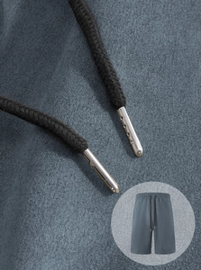 Macro detail of men's casual shorts showing woven drawstring with metal tips in grey blue