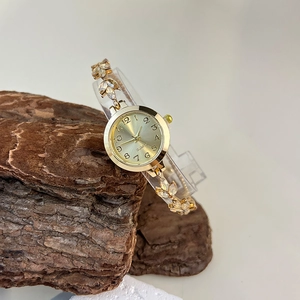 Close-up of gold quartz watch with leaf-shaped crystal links on white and wood base