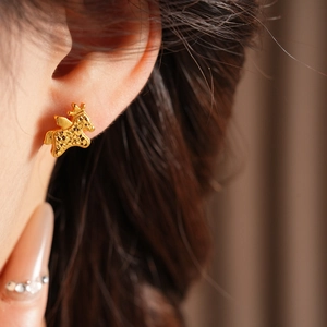 Close-up of gold unicorn stud earrings with crown detail on ear of the model