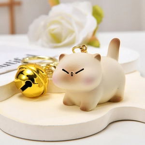 Close-up of cute Siamese cat keychain with beige resin body and a large golden bell