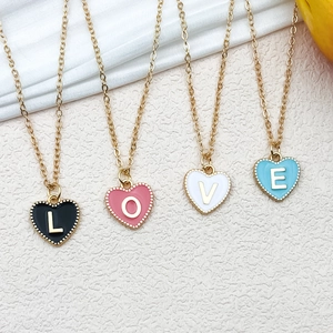Detail of four gold enamel heart pendants spelling LOVE on textured fabric backdrop
