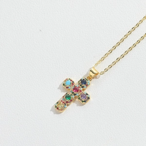 Detail of a gold cross necklace pendant set with colorful vibrant multi-colored gemstones