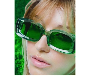 Close-up of green rectangular thick-frame sunglasses worn by a model in nature