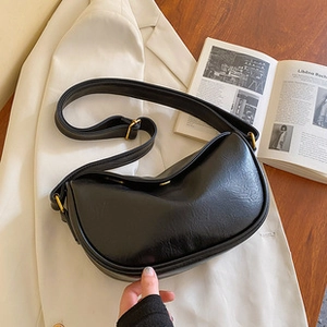 Detail of black leather crescent bag with golden hardware on a white blazer
