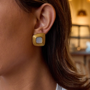 Gros plan de boucles d'oreilles carrées dorées avec résine blanche sur un mannequin