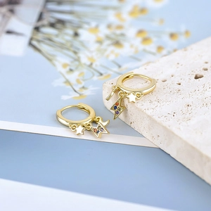 Macro detail of gold hoop earrings with star and colorful crystal lightning bolt charms