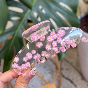 Close-up of pink floral acrylic hair claw clip held by hand in natural light