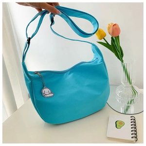 Blue dumpling crossbody bag detail with cartoon sheep pendant on a white desk setup