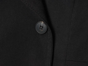 Macro shot of black twill fabric texture and dark grey resin button detail on blazer