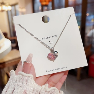 Gros plan du pendentif cœur en cristal rose et pierres sur carte de remerciement