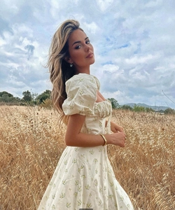 Detail of puff sleeves and floral pattern on a cream French midi dress in a sunny field