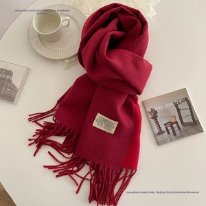 Close-up of deep red cashmere-feel scarf with fringe and label in a cozy winter setting