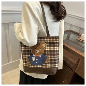 Detail of checkered canvas tote bag featuring brown teddy bear patch and PU leather strap