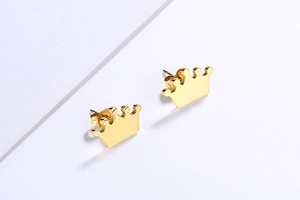 Macro detail of trendy golden crown stud earrings featuring a polished metallic finish