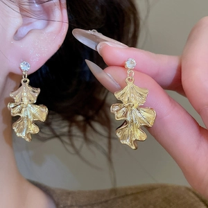 Detailed view of golden ginkgo leaf earrings with crystal studs worn by a model