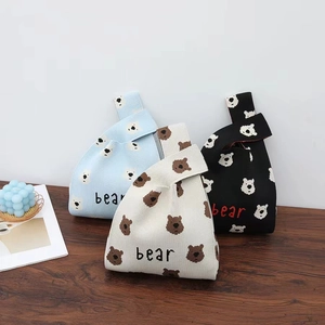Detail of knitted tote bags with bear patterns in blue, cream, and black on a wooden table