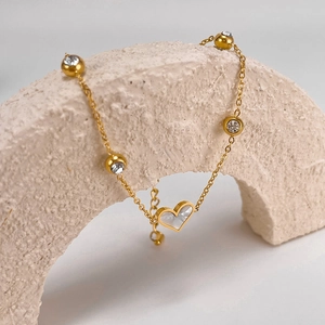 Detail of golden heart bracelet with zircons draped on a white textured stone arch