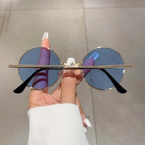 Détail de lunettes de soleil rondes en métal doré avec verres bleu clair tenues à la main