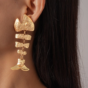 Close-up of a golden fishbone drop earring with hammered texture on a female model