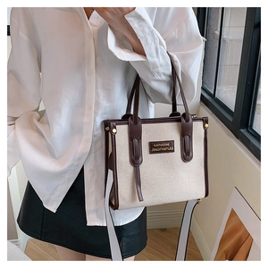 Detail of beige canvas tote with dark brown leather trim held by a model in a natural setting