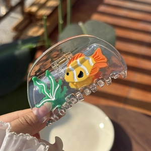 Close-up of a clear fish tank hair claw clip with colorful goldfish and seaweed patterns