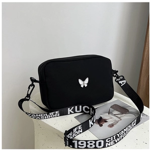 Detail of black nylon crossbody bag with silver butterfly emblem and printed strap
