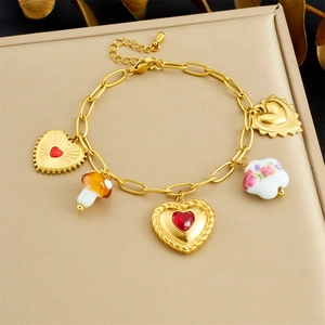 Detail of a gold chain bracelet featuring a red gemstone heart and mushroom charms
